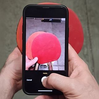 Hand holding smartphone taking a photo of red ping pong paddles on the ground